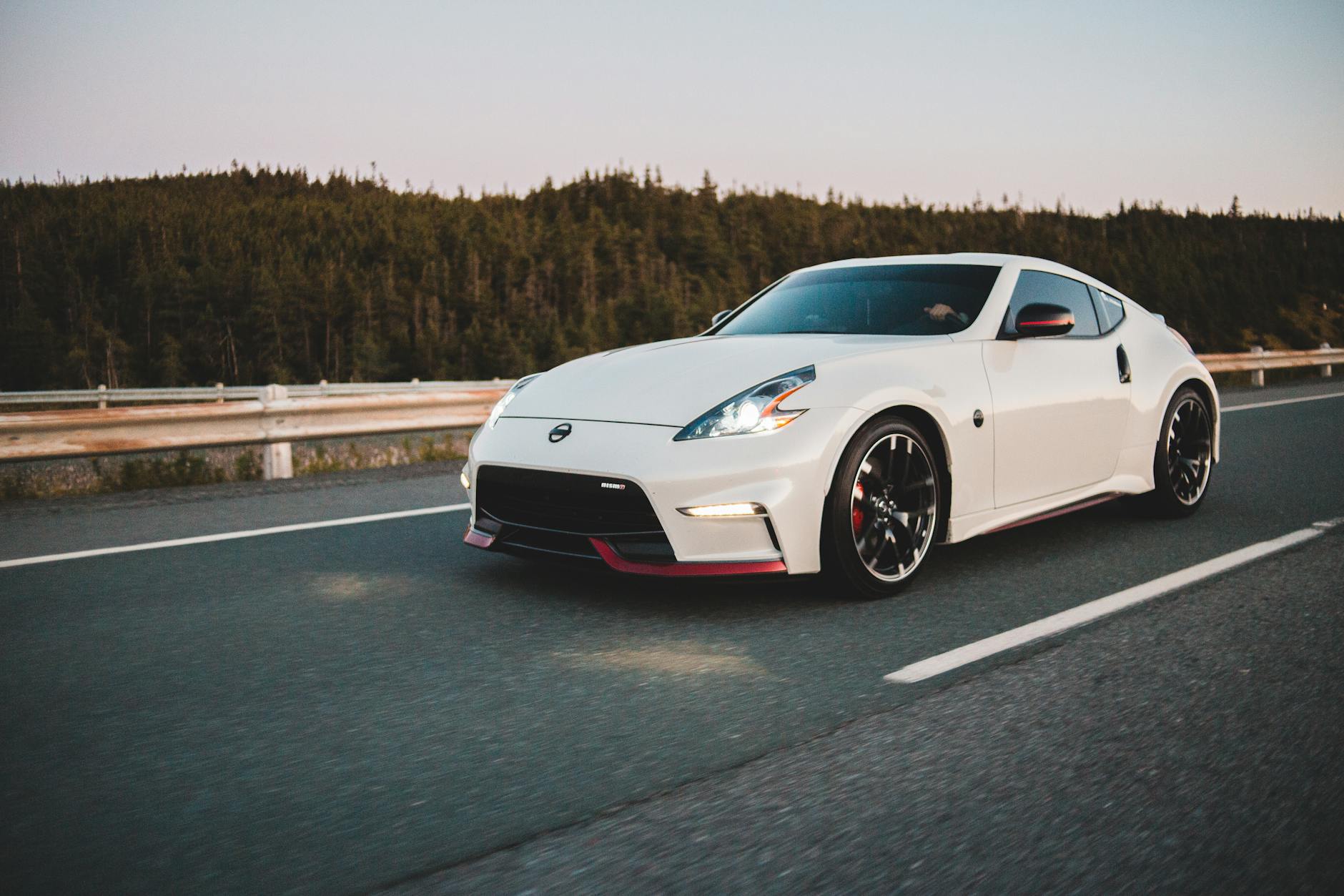 Czerwone Ferrari jedzie o zmierzchu drogą wśród zielonych drzew