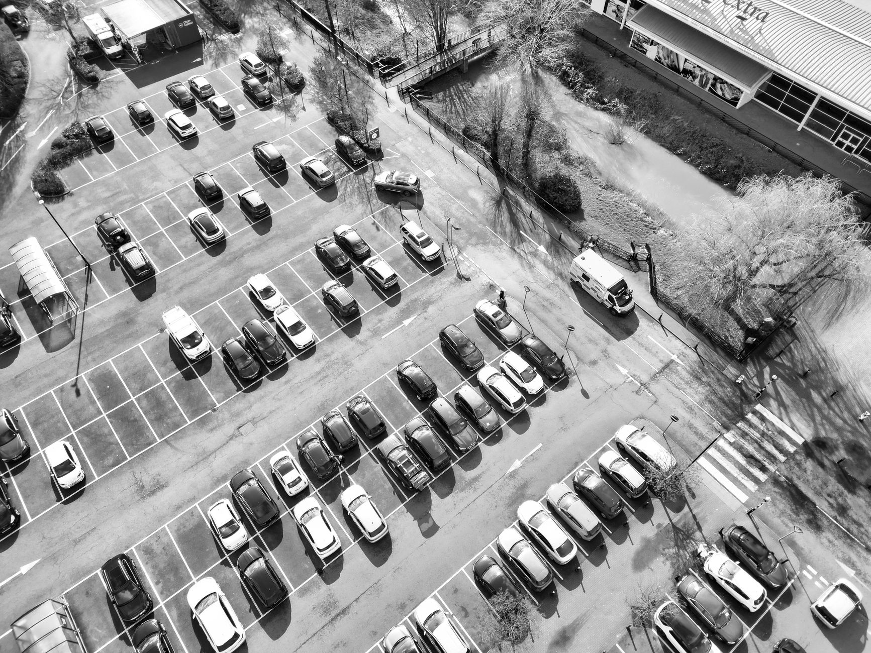 Czarno-białe zdjęcie parkingu przed sklepem z wieloma zaparkowanymi autami